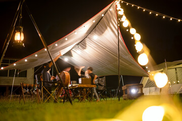 Night camping scenes, long exposures in moving parts are blurry..Night camping with tent accommodation and relaxation seats, with an Asian family having dinner, playing guitar and having fun.