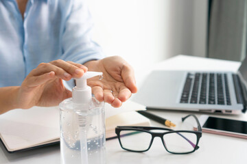 Asian businesswoman working at workplace and apply hand sanitizer gel onto her hand to disinfect germs. Working from home, health care and new normal lifestyle concept. Closeup, copy space