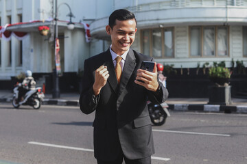 Happy man looking at his smartphone and raising his arm up to celebrate success or achievement.