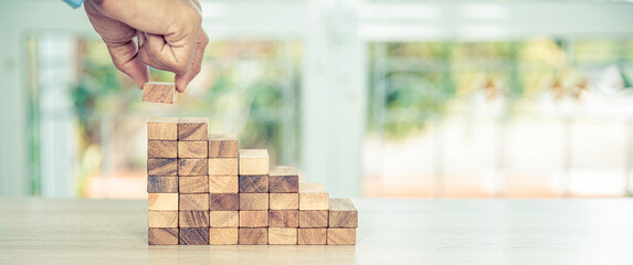 Hand placing wooden block tower stack in pyramid stair step with caution to prevent collapse or...