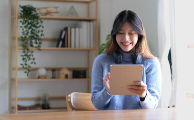 Portrait of smiling happy beautiful asian woman relaxing using technology of tablet while sitting on table.Young creative girl working and typing on keyboard at home.work at home concept