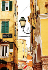 Blick in eine typische Gasse in Korfu-Stadt, eine alte Laterne zwischen den H&auml;usern im Mittelpunkt, vertikal 