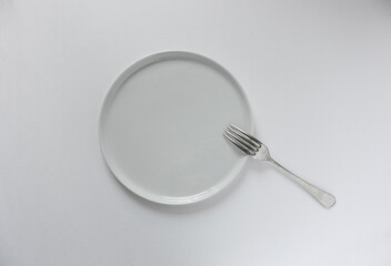 Flat white plate with no rim and fork on white background.