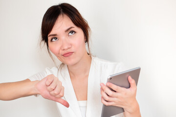 Upset angry asian woman using computer tablet showing rejecting thumb down gesture