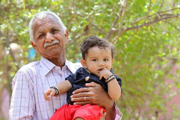 Portrait photo of Indian Senior grandfather with toddler grandson looking at camera with blur background