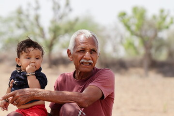 Portrait photo of Indian Senior grandfather with toddler grandson siting in nature and playing outdoor , Rajasthan India