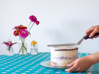 Woman spreading the icing to cover the top of the cake. Home baking, handmade. Free time on quarantine. Female hands level the cream with a spatula and cover the round cake with butter cream. DIY. - obrazy, fototapety, plakaty