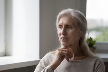 Anxious frustrated lonely senior 70s woman concerned with bad news, feeling depressed, worried, going through grief, health problems, mental disorder, disease, looking away, touching chin, thinking