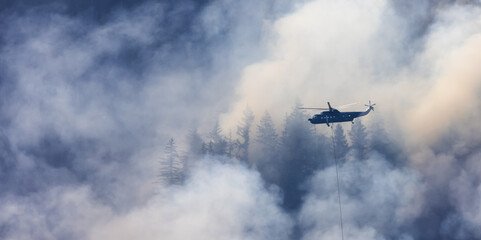 Wildfire Service Helicopter flying over BC Forest Fire and Smoke on the mountain near Hope during a hot sunny summer day. British Columbia, Canada. Natural Disaster