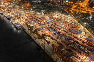 Aerial view of container cargo ship in the export and import business and logistics international goods in urban city. Shipping to the harbour by crane in Bangkok harbour, Thailand at night.