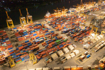 Fototapeta premium Aerial view of container cargo ship in the export and import business and logistics international goods in urban city. Shipping to the harbour by crane in Bangkok harbour, Thailand at night.