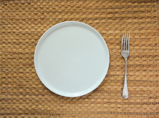 white plate and fork on seagrass place mat