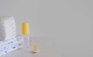 stack of nappies, baby bottle and nipple on a white wooden table. empty copy space. newborn care background