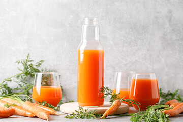 Carrot juice in a glass and bottle and fresh carrots with leaves