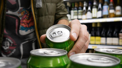 Close-up of a male buyer's hand taking a green can of beer in alcohol department