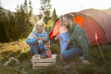 Couple with little girl have picnic at campsite while traveling with tent in the mountains. Young...
