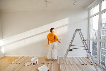 Woman paints the wall in white color while making repairment in newly purchased apartment. Repair...