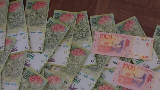 billetes de 1000 pesos argentinos caen sobre un colchon de billetes 500 pesos sobre fondo de madera marron