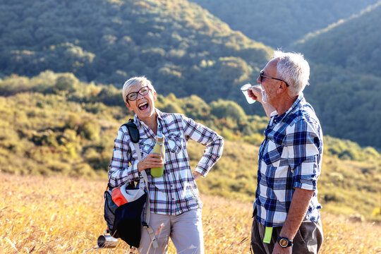 Two senior adult have pause on hiking and drink water and smile in natural environment