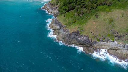 Aerial view of sea waves crashing on rocks cliff in the blue ocean. Top view of coastal rocks in Phuket ocean. Landscape view point of Laem Phromthep Cape in the morning.