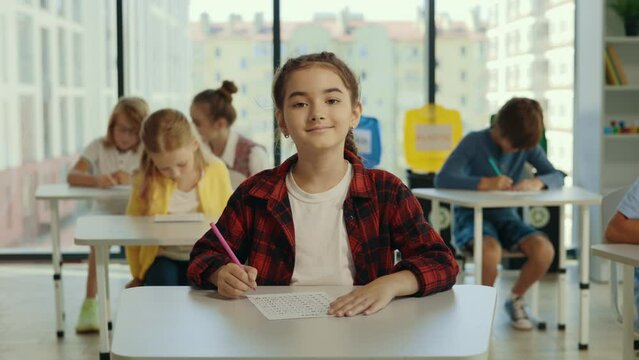 Exam in prime school. Portrait pupil girl looking at the at the camera in the classroom against the background of children. Elementary school. Learning and education concept.