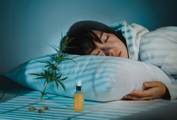 Asian girl sleeping in evening bedroom with cbd oil, capsules and a cannabis branch. Melatonin...