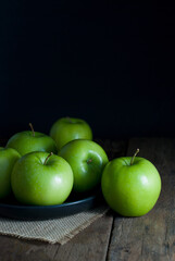 Delicious green apples in a black ceramic tray put on sackcloth on a rustic wooden floor.