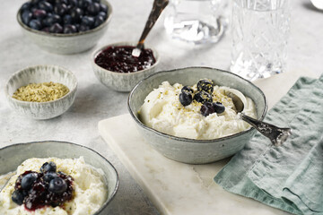 Two grey bowls with plain white icelandic diary breakfast skyr with jam, fresh blueberries, hemp seeds on marble board on grey background