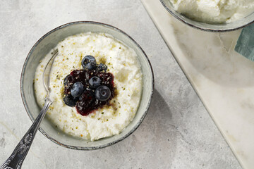 Two grey bowls with plain white icelandic diary breakfast skyr with jam, fresh blueberries, hemp...