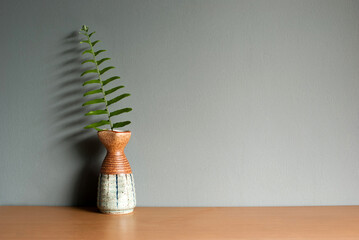 Fern leaves in a ceramic vase on a wooden table and grey background with copy space.
