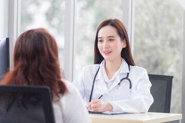 Asian woman who wears medical coat and stethoscope talks with woman patient to consult and suggest healthcare information in hospital.