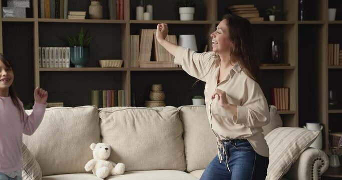 Happy excited little daughter kid and active young mom having fun together, dancing to music. Nanny entertaining child, teaching to dance, warming up for exercising. Indoor activity concept