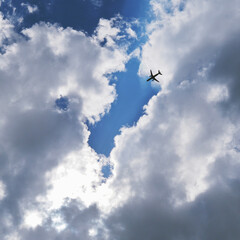 The passenger airplane is flying far away in the blue sky and clouds. Dramatic clouds with the sun shining through them. Aircraft in the air. Square illustration. Passenger air transportation