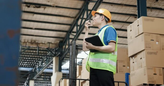 Man, manager or supervisor with hard hat, vest to hold check list, walkie-talkie in distribution warehouse. To check stock, inventory, cargo, box on racking, shelf. Concept for business and industry.
