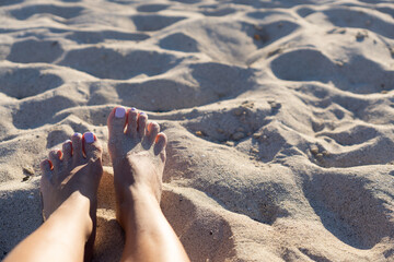 Close-up of legs and feet in the sand on the beach, with painted nails and tanned legs with copy space.