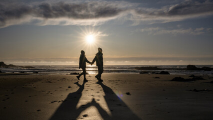 Couple holding hands, walking on the beach at sunrise.  Catlins, South Island.