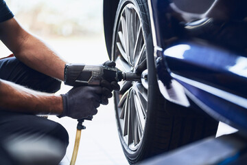 Closeup of car mechanic changing car wheel tire with pneumatic wrench in auto service