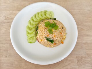 chicken fried rice and sliced ​​cucumber on a white plate, Thai food, wooden table