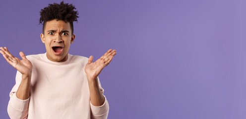 Close-up portrait of displeased, bothered frustrated hispanic man spread hands sideways in dismay and confusion, staring camera upset with disappointed grimacing expression, purple background