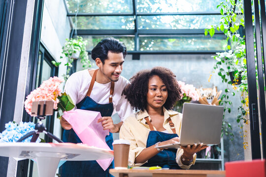 Asian male and  African female florists flower store owners working and doing inventory. Man typing on laptop at desk in floral shop . Business concept