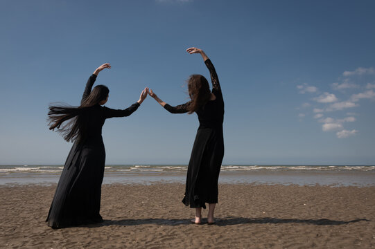 fine art portrait of mother and daughter in black dresses dancing on the beach