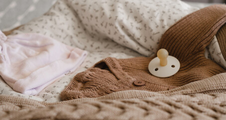 Fototapeta na wymiar knitted brown baby romper and nipple, pink hat and toy on warm knitted blanket. autumn set of baby clothes. selective focus