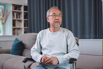 Fototapeta premium Asian senior elderly mature man feel stress headache sitting on wheelchair in living room. Old man touching his temples from horrible migraine. Health care and medical insurance concept.