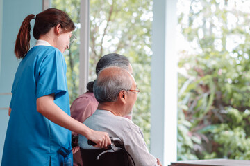 Obraz premium Asian caregiver nurse support senior elderly man on wheelchair in living room. nurse female take care of mature patient doing physical therapy at nursing home. Health care concept.