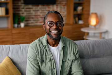Headshot of cheerful adult african american man in glasses and casual relaxing on sofa