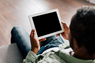 Mature african american male watching video on tablet with empty screen, sit on sofa in living room