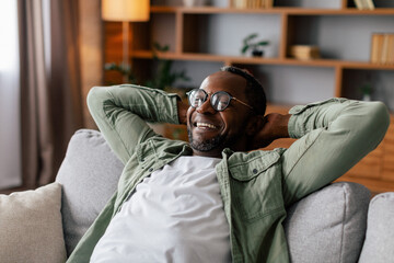 Satisfied adult african american man in glasses and casual resting and relaxing, enjoy comfort,...