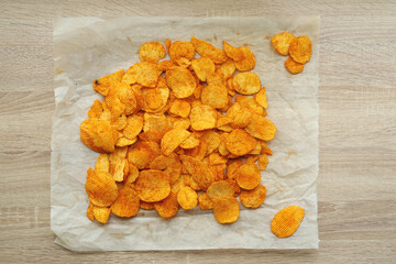 Top view dry potato chips with paprika on a sheet of paper on the kitchen table.