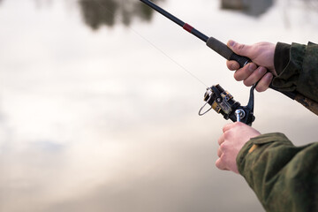 The fisherman's hands rotate the spinning reel against the background of the pond water. Background. Selective focus
