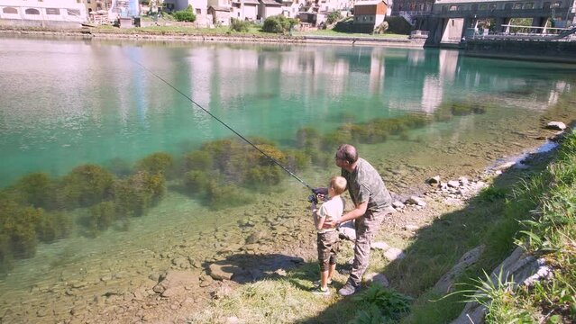 father and son are fishing together in a beautiful mountains's lake